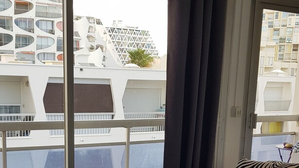 Un salon moderne avec une table basse en verre, un canapé à motifs zébrés et une vue sur le paysage urbain, visible à travers de grandes fenêtres.
