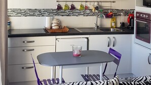 Une cuisine moderne avec des meubles blancs, un plan de travail noir et un coin repas agrémenté d’un canapé à motifs zébrés.