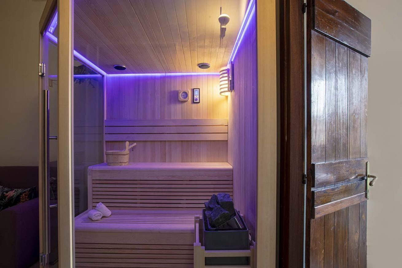 A sauna with wooden benches, a bench with towels, and a container with stones.