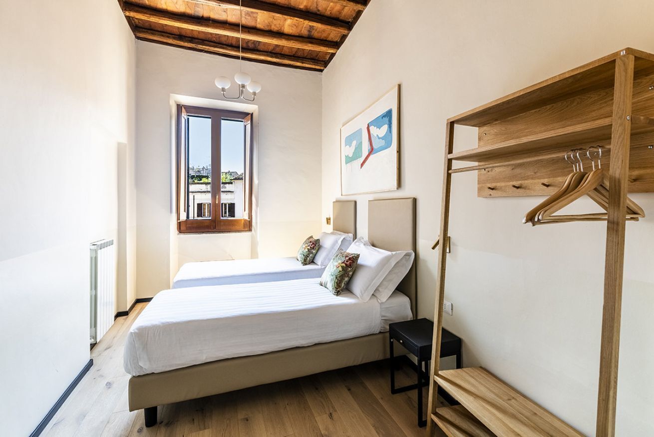 A bedroom with a bed, a wooden bench, a hanging coat rack, and a window with a view.