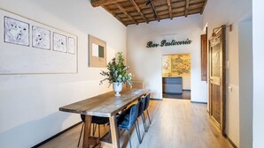 Zona pranzo con tavolo e sedie in legno, una pianta in vaso e un cartello con su scritto 'Bar Pasticceria'.
