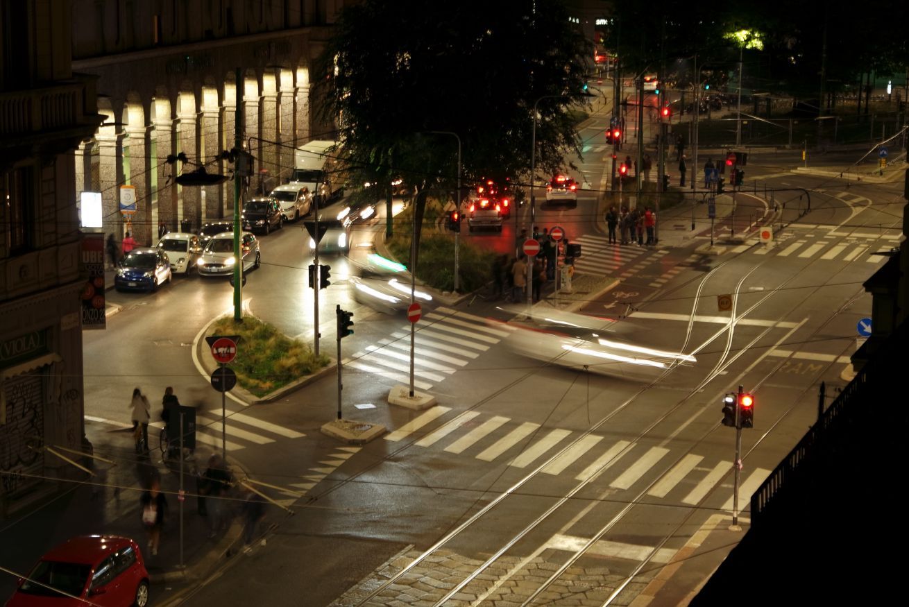 Cruzamento urbano noturno com semáforos, veículos e pedestres.