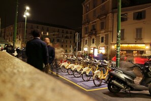 A nighttime street scene with a row of parked bicycles and a scooter, buildings in the background, and a gelateria sign.