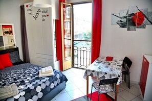 A bedroom with a bed, a desk, and a balcony.