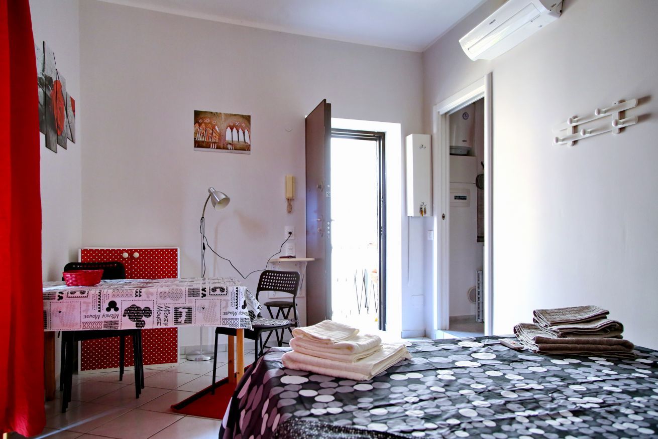 Un dormitorio con una cama, un escritorio, una silla, una mesa y una puerta que da a otra habitación.