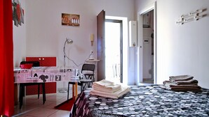 Une chambre à coucher comprenant un lit, un bureau, une chaise, une table et une porte donnant sur une autre pièce.