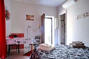 Une chambre à coucher comprenant un lit, un bureau, une chaise, une table et une porte donnant sur une autre pièce.
