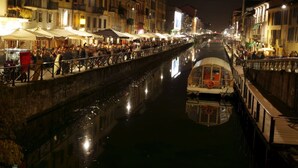 Une promenade le long du canal, bordée de bâtiments des deux côtés, avec un bateau amarré sur la droite et des personnes qui se promènent le long du sentier.
