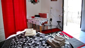 A room with a bed, a table with a polka dot tablecloth, a chair, a red curtain, and a door leading outside. - Nice and bright apartment with wi-fi and a/c in Darsena and Navigli district (Milano)