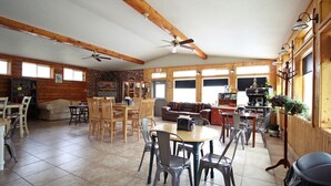 Un vaste espace de vie doté d’une cheminée, de poutres apparentes en bois au plafond et d’un coin repas avec des chaises et une table.