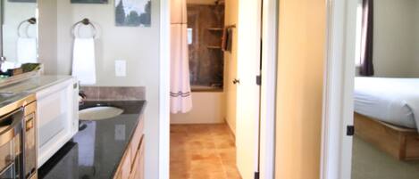 A narrow hallway with a kitchen area on the left, a bathroom with a shower and toilet, and a bedroom with a bunk bed on the right.