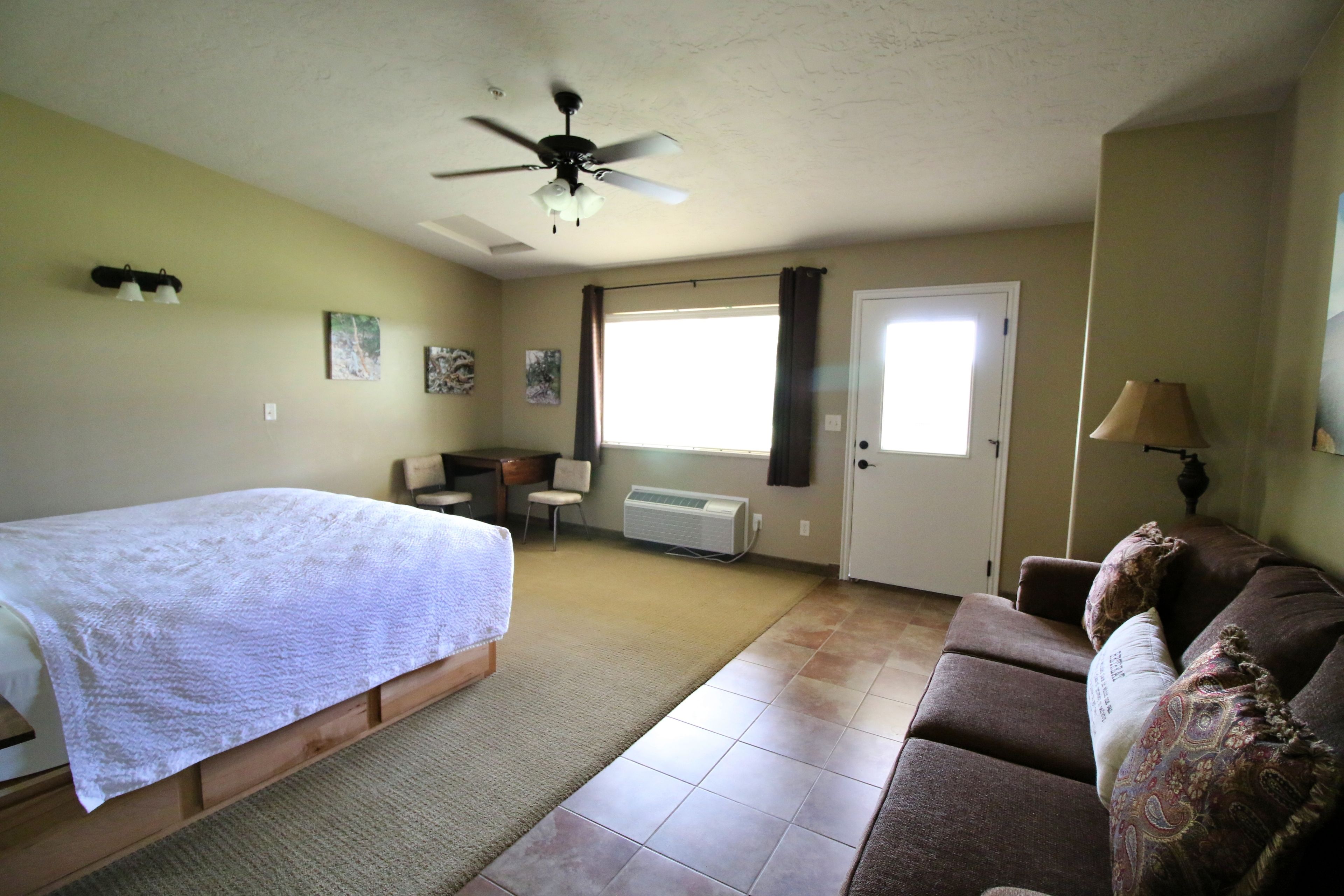 Une chambre à coucher avec un lit, un ventilateur de plafond, une fenêtre, un canapé et une porte.