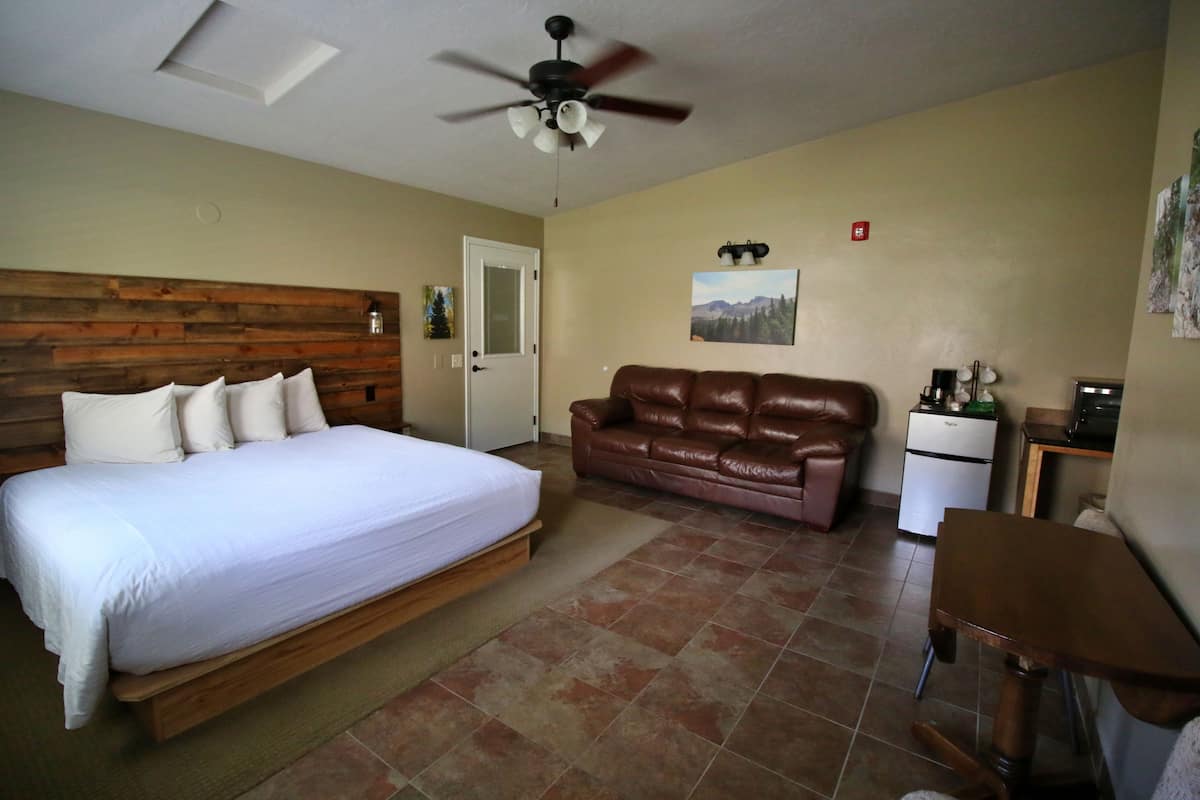 A bedroom with a bed, a brown leather sofa, a small desk, and a ceiling fan.