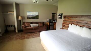 A bedroom with a bed, a wooden headboard, a brown sofa, a ceiling fan, a TV, and a wall-mounted shelf.