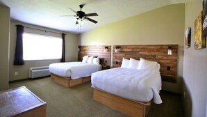 Une chambre d’hôtel avec deux lits simples, un ventilateur de plafond, une grande fenêtre avec des rideaux et une tête de lit en bois.