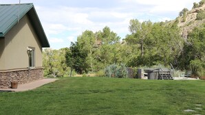 Une maison avec des fondations en pierre et un toit végétalisé, entourée d’une pelouse bien entretenue et d’arbres.