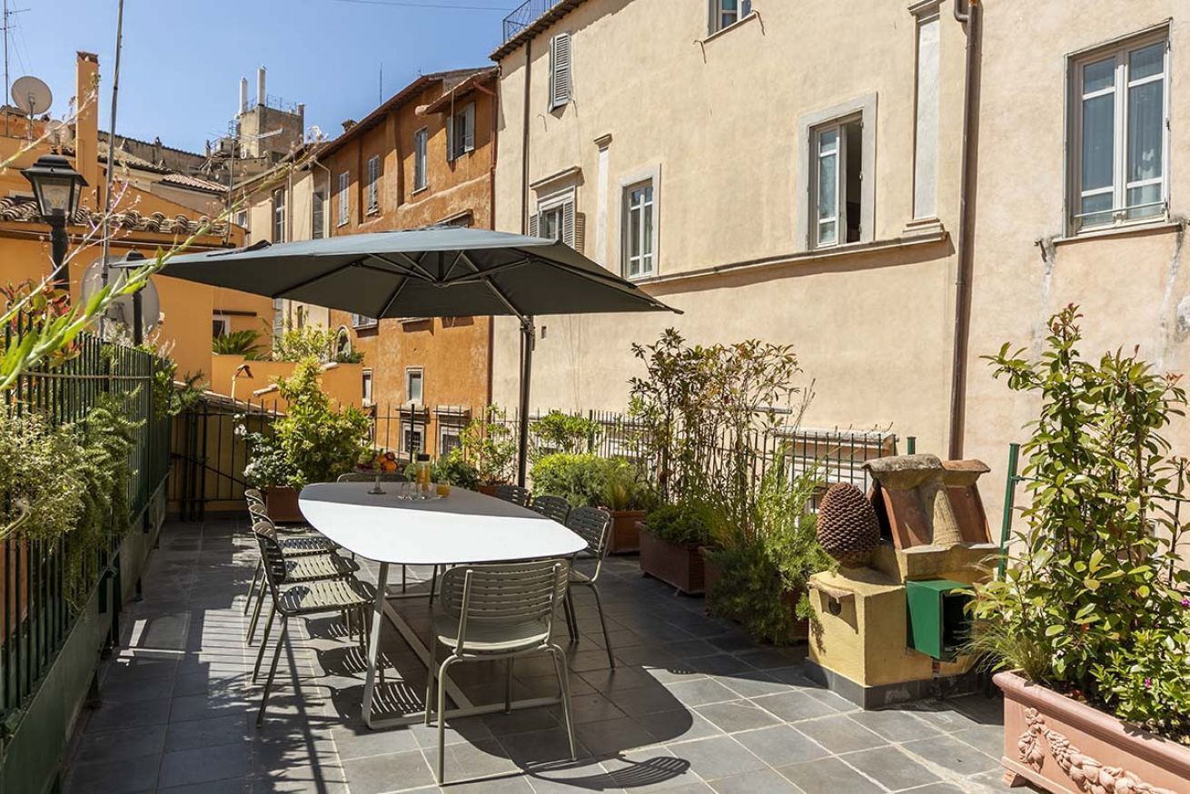 A patio with a table and chairs, surrounded by potted plants and a decorative stone structure.