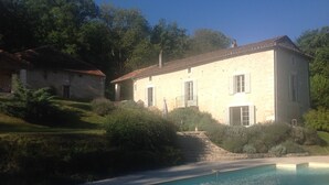 Una casa de dos pisos con piscina, rodeada de follaje y árboles.