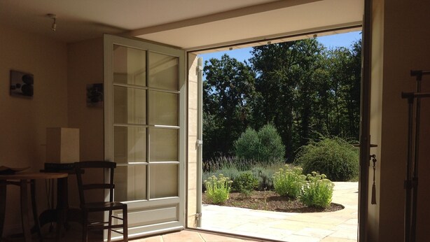 Una habitación con puerta de vidrio corredera que da a un patio exterior con jardín y suelo de baldosas.