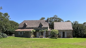 A stone house with a tiled roof, a small garden, and a clear blue sky.