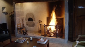 A stone fireplace with a fire burning inside, surrounded by rustic furniture and a bookshelf.