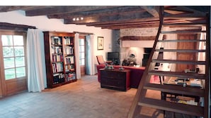 A rustic room with exposed wooden beams, a fireplace, a bookshelf, and a red sofa.