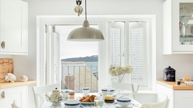A dining area with a table set for breakfast, a view of the sea through a window, and a hanging light fixture.