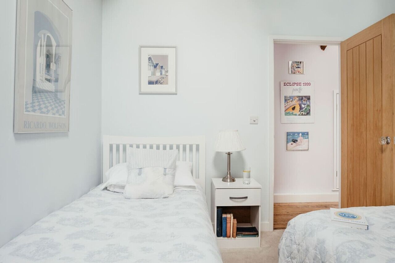 A bedroom with two beds, a nightstand with a lamp, and a wooden wardrobe.