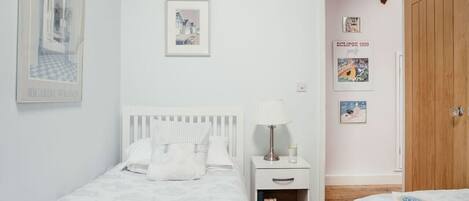 A bedroom with two beds, a nightstand with a lamp, and a wooden wardrobe.