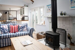 A cozy living room with a striped sofa, a wooden table, and a black wood stove.