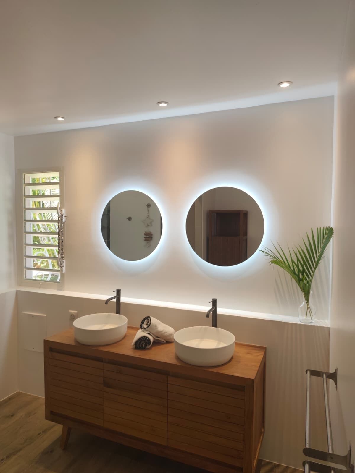 Un baño con dos espejos redondos, un tocador de madera y una ventana con persianas.