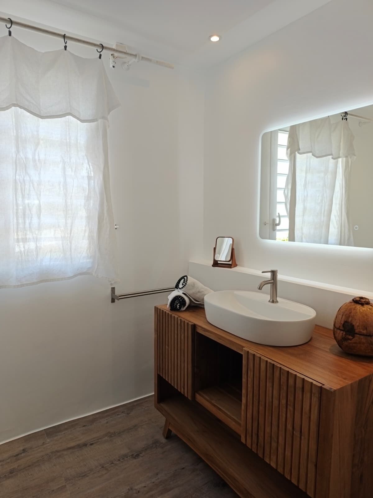 A bathroom with a white sink, wooden vanity, a mirror, a towel rack, and a shower curtain.