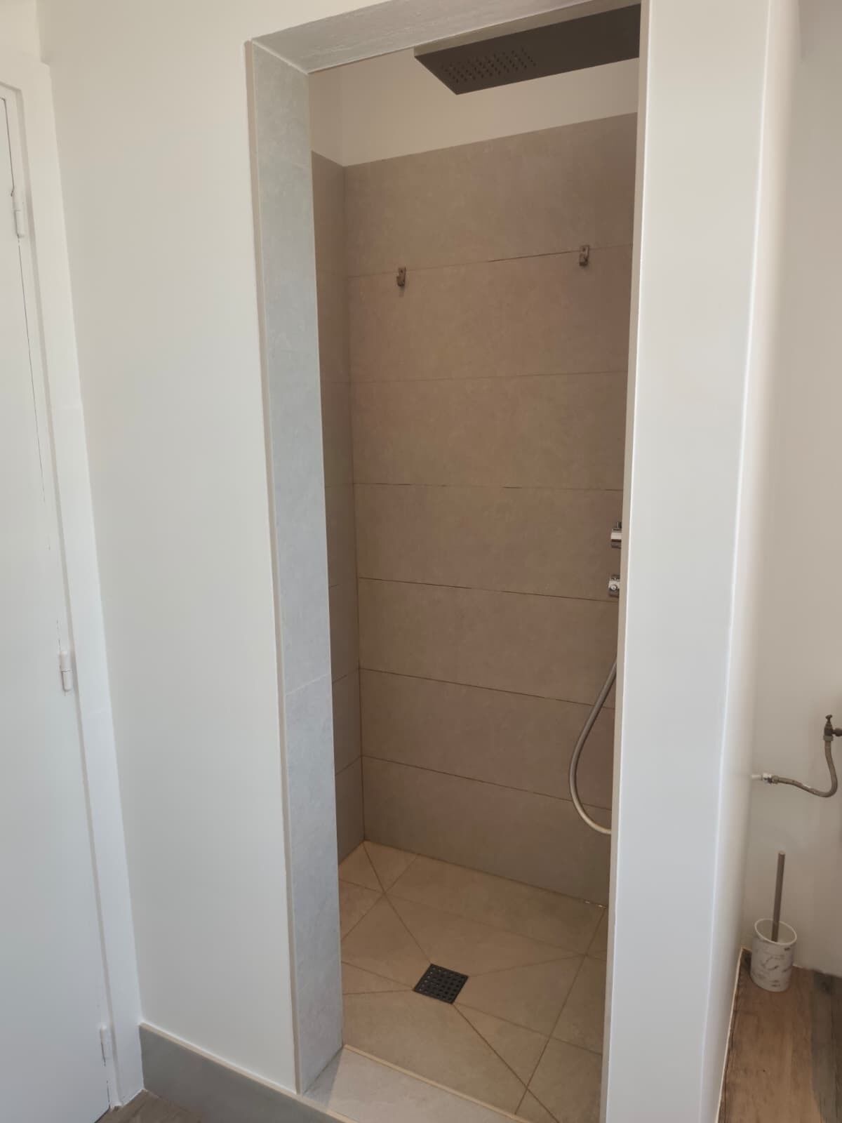 A small, enclosed shower area with tiled walls and floor, a drain, and a handheld showerhead.