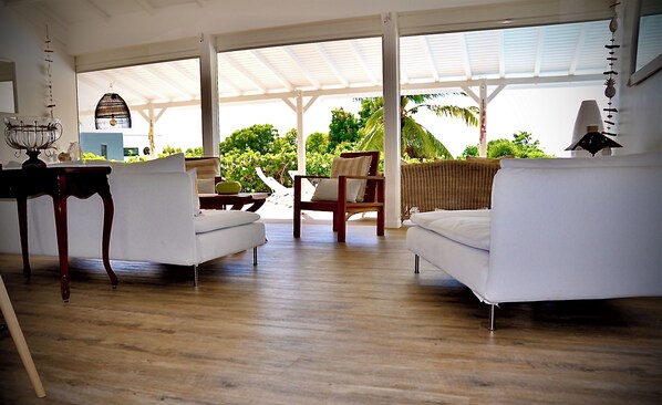 A spacious room with a wooden floor, white sofas, a wooden table, and a hanging light fixture. - villa MAGAR standing overlooking the sea Pool and Jacuzzi (Le Gosier)