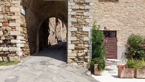 A stone archway leading to a building with a wooden door and potted plants. - Medieval village flat, second floor with Wi-Fi & aircon (Compignano)