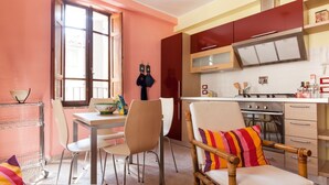 A compact kitchen with a dining area, featuring a wooden table, chairs, and a modern stove. - Medieval village flat, second floor with Wi-Fi & aircon (Compignano)