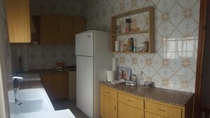 Uma cozinha com armários de madeira, uma geladeira branca, bancada com diversos objetos e painel de azulejos.