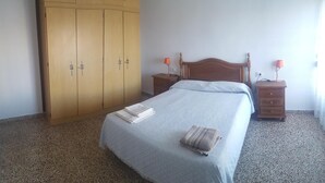 Quarto com cama, guarda-roupa, duas mesas de cabeceira com luminárias e piso coberto por carpete.