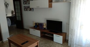 Una sala de estar con una mesa de centro de madera, un televisor de pantalla plana sobre un mueble de madera y un estante pequeño con adornos.