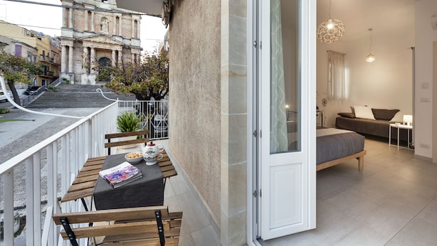 A balcony with a table and chairs, a bed, and a view of a historic building. - Piazza Salvatore, 7, rooms with a view (Ragusa)