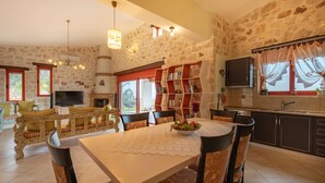 Een ruime woonkamer met een stenen muur, een open haard, een televisie en een eettafel met stoelen.