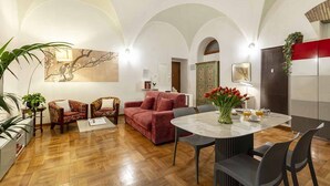 Ein geräumiges Wohnzimmer mit Holzboden, einem roten Sofa, einem runden Tisch mit Stühlen und einem großen Gemälde an der Wand.
