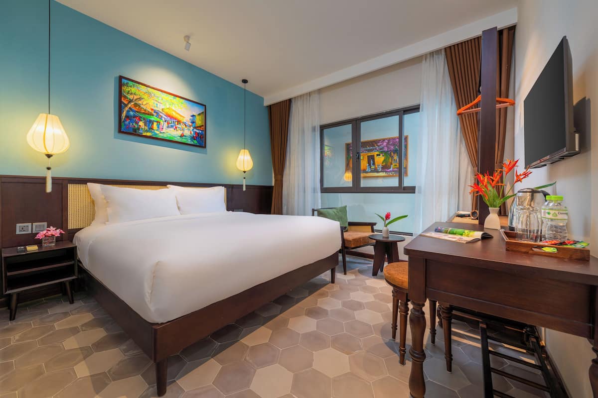 A hotel room with a large bed, a desk, a chair, a TV, and artwork on the walls.
