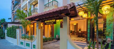 Entrada de un hotel con un letrero que dice 'BACKHOME BOUTIQUE', un suelo de baldosas y un piso a cuadros.