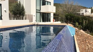 En moderne bygning med en swimmingpool, omgivet af et klippefyldt landskab og sparsom vegetation.