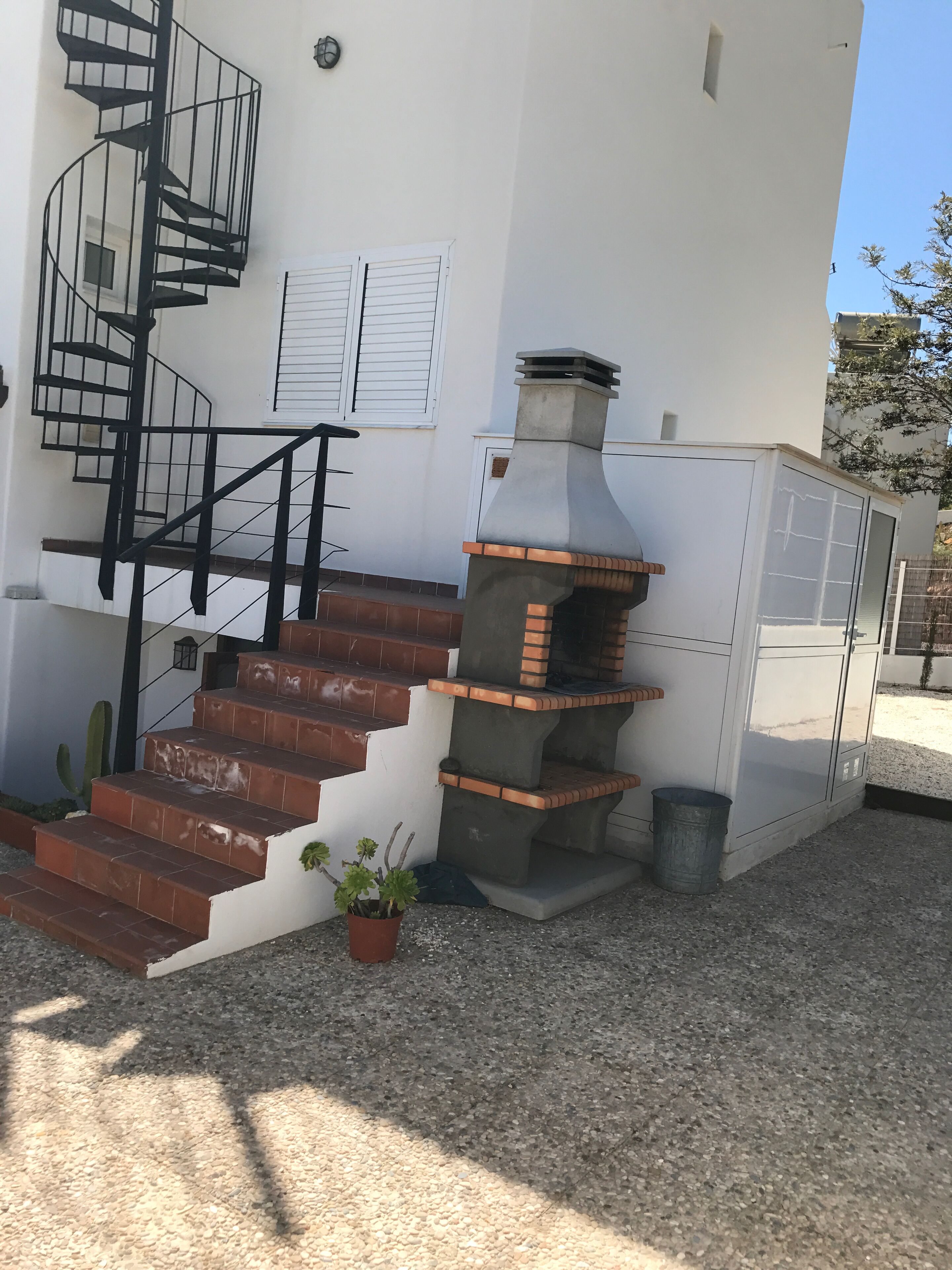 A building with a spiral staircase, a brick oven, and a potted plant.