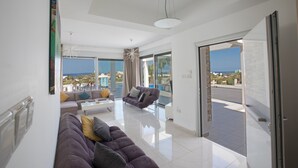 A modern living room with a large sofa, a coffee table, and a view of the pool and ocean.