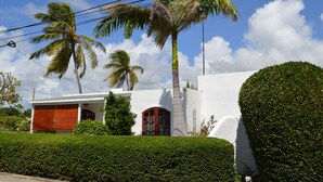 Un bâtiment blanc avec une porte rouge, entouré de haies bien entretenues et de palmiers.