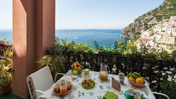 A balcony with a table set for breakfast, overlooking a coastal town and the sea. - Casa Annalu with sea view - My Rental Homes (Positano)