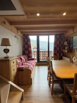 Une pièce chaleureuse avec un plafond en bois, un canapé, une table à manger et un téléviseur.